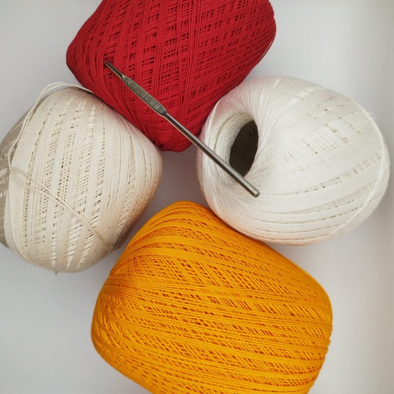 Quatre pelotes de laine (rouge, blanc, crème, jaune) et un crochet.